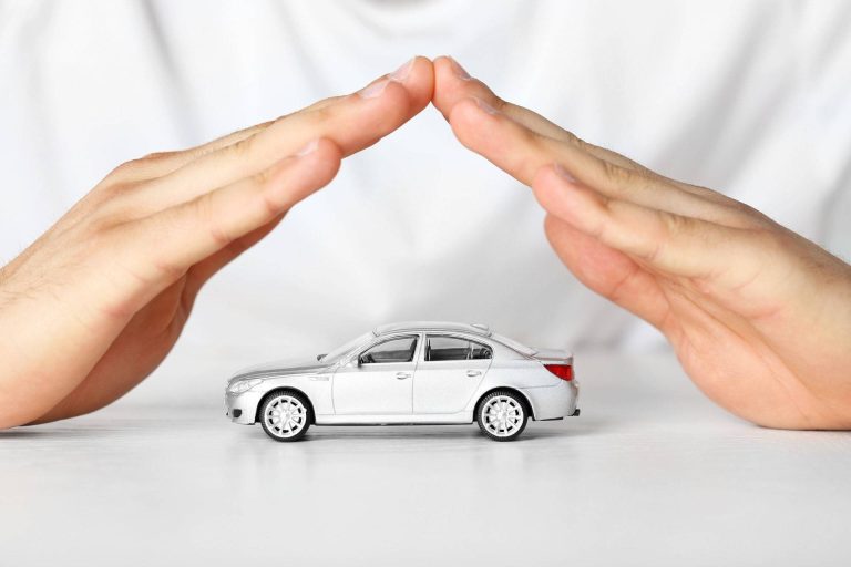 تصویری از دست‌هایی که به طور خلاقانه بر فراز یک ماشین اسباب بازی سفید قرار گرفته‌اند تا آن را در بین انگشتان خود نگه دارند. این تصویر نمادی از بیمه بدنه خودرو است.