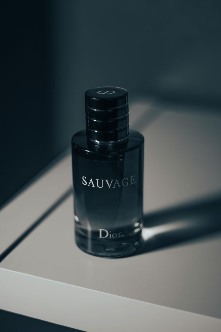 یک بطری سیاه از ادکلن dior sauvage که بر روی میز سفیدی قرار دارد و سایه ی آن بر روی میز منعکس شده است