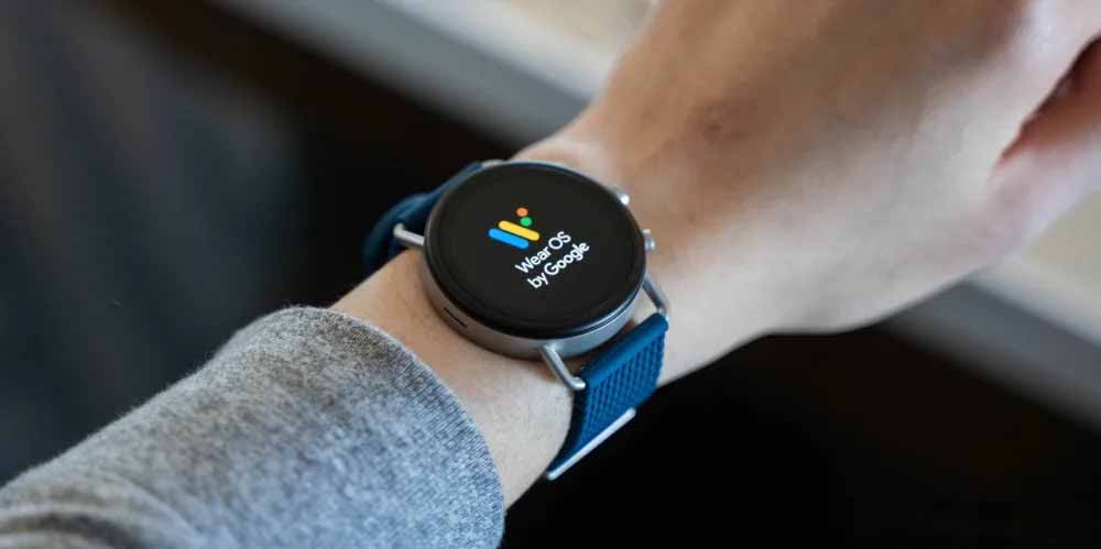 تصویری از یک دست که یک ساعت هوشمند روی آن بسته است که روی آن نوشته وار اس بی گوگل 